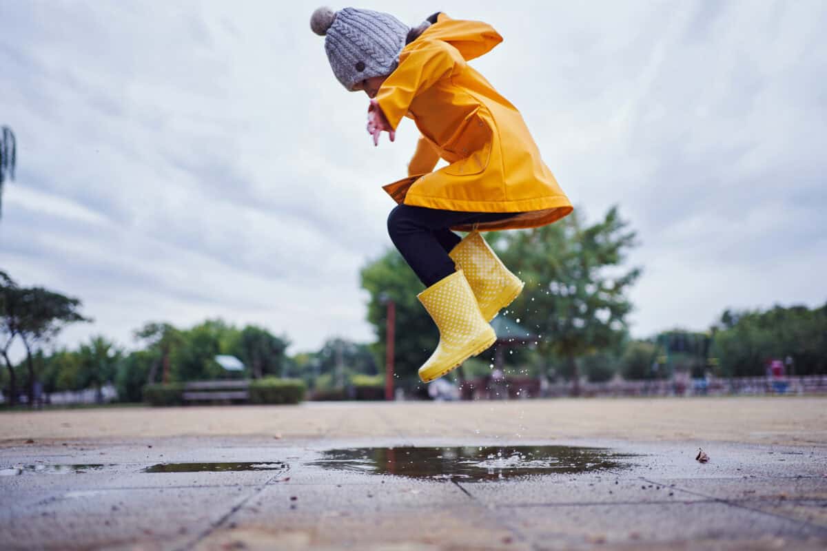 child in yellow raincoat joyfully jumps into rain puddle