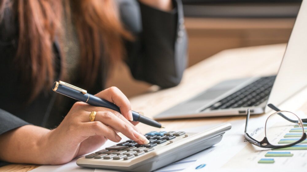 edit Woman calculating numbers next to laptop